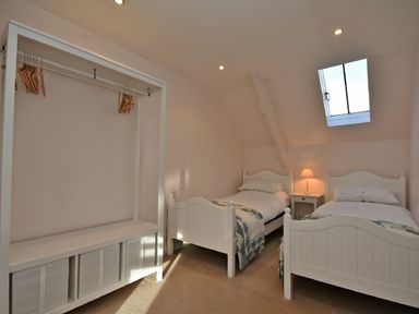 A bedroom with two white single beds a nightstand with a lamp and an open clothing rack at Croft Cottage in Alnwick