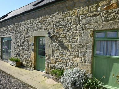 Stone exterior wall with green doors and windows and plants outside at Croft Cottage in Alnwick