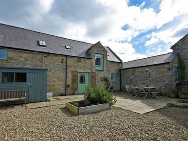 An outdoor courtyard with gravel ground a wooden raised planter and outdoor dining table with chairs at Croft Cottage Alnwick