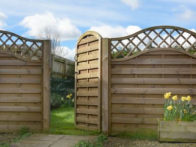 A wooden garden gate open to a grassy yard with yellow flowers at Croft Cottage in Alnwick