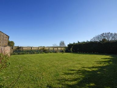 A grassy backyard with a wooden fence and trees at Croft Cottage in Alnwick