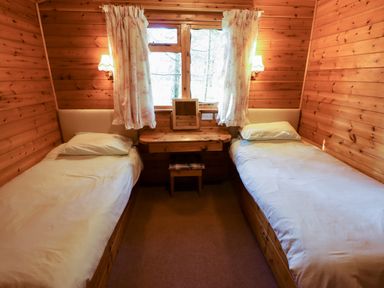 A bedroom with two single beds a window with curtains and a small wooden desk with a stool at Kestrel in Withern near Alford