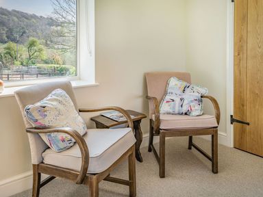 Two wooden armchairs with cushions a small wooden side table and a window showing a hillside outside at Pant Y Cwtsh in Kidwelly
