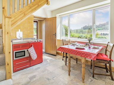 A kitchen with a red stove and microwave a wooden dining table with a red polka dot tablecloth and two chairs near a window at Pant Y Cwtsh in Kidwelly