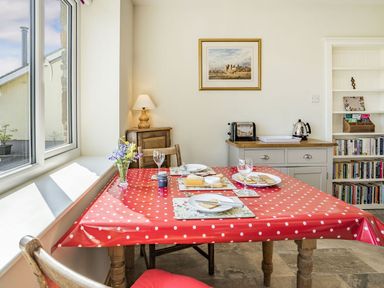 A dining area with a red polka dot tablecloth on a table set with plates cheese and crackers a lamp on a wooden cabinet a bookshelf and a kettle on a counter at Pant Y Cwtsh in Kidwelly