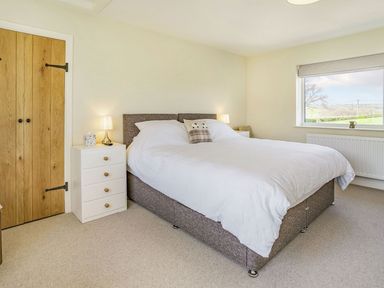 A bedroom with a double bed two bedside tables with lamps a white chest of drawers and a window showing a countryside view at Pant Y Cwtsh in Kidwelly