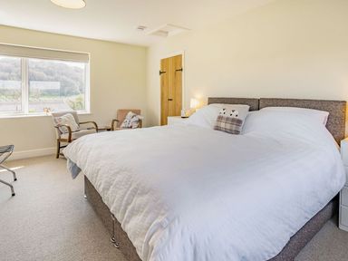 A bedroom with a large bed a window two armchairs and a wooden door at Pant Y Cwtsh in Kidwelly