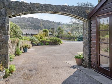 A stone archway over a driveway with potted plants and a wooden door on the right at Pant Y Cwtsh in Kidwelly