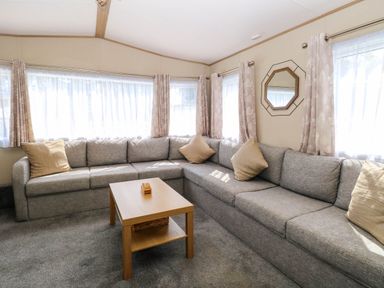 A living room with a gray corner sofa beige cushions a wooden coffee table and windows with curtains at Oakley Retreat in Fritton near Belton