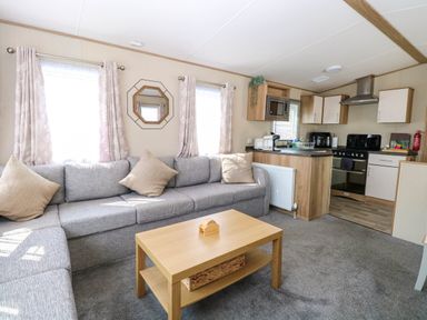 A living room with a gray sofa beige cushions a wooden coffee table and a kitchen with wooden cabinets at Oakley Retreat in Fritton near Belton