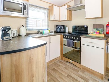 A kitchen with white and wood cabinets a microwave coffee machine kettle oven and sink at Oakley Retreat in Fritton near Belton