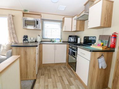A kitchen with wooden cabinets a microwave a coffee machine and a stove at Oakley Retreat in Fritton near Belton