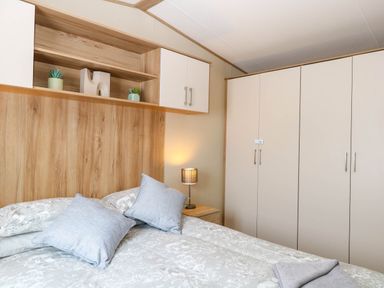 A bedroom with a bed topped with pillows and blankets next to a nightstand with a lamp and a wardrobe in Oakley Retreat in Fritton near Belton