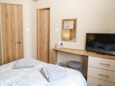A bedroom with a bed with towels on it a wooden desk with a television and a mirror on the wall oakley retreat fritton near belton