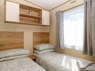 A bedroom with two single beds with patterned bedding a window with curtains and a wall-mounted cupboard at Oakley Retreat in Fritton near Belton