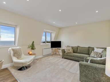 A living room with green sofas a white chair and windows showing sea views at No 10 Croft House in Tenby