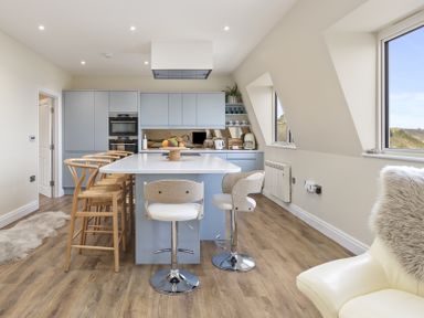 A kitchen with light blue cabinets a white island with stools wooden chairs and large windows with views at No 10 Croft House in Tenby