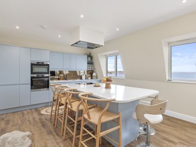 A kitchen with blue cabinets wooden chairs and two windows overlooking the sea at No 10 Croft House in Tenby