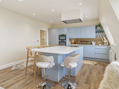 A kitchen with blue cabinets a white island with stools wooden chairs and appliances at No 10 Croft House in Tenby