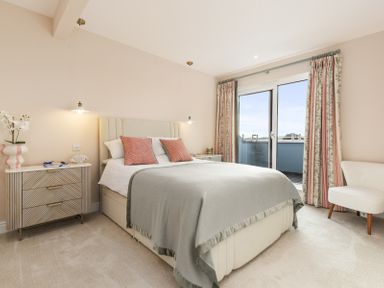 A bedroom with a bed bedside tables a chair and a sliding glass door with curtains at No 10 Croft House in Tenby