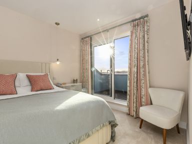 A bedroom with a bed with two pillows a bedside table a hanging light a chair and sliding glass doors with curtains at No 10 Croft House in Tenby