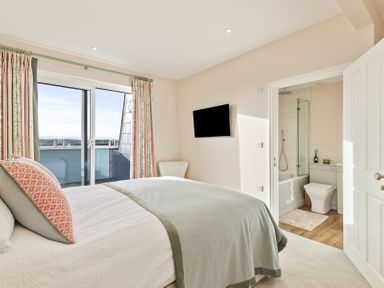 A bedroom with a bed a wall-mounted tv curtains on a sliding door and an ensuite bathroom at No 10 Croft House in Tenby