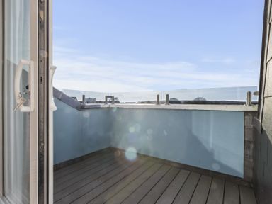 A small outdoor balcony with glass railings and wooden flooring at No 10 Croft House in Tenby