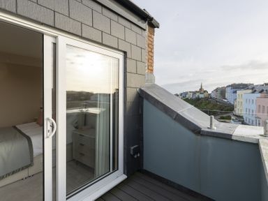 A balcony with sliding glass door leading to a bedroom and view of buildings and a church spire at No 10 Croft House in Tenby