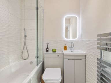 A bathroom with a bathtub shower glass panel toilet sink cabinet illuminated mirror and heated towel rail at No 10 Croft House in Tenby