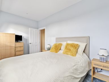 A bedroom with a bed with yellow pillows bedside tables a lamp a chest of drawers and a small television at No 10 Croft House in Tenby