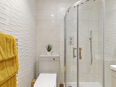 A bathroom with a toilet, corner shower with glass doors, yellow towels on a heated rail, and a small plant on the toilet tank at No 10 Croft House in Tenby
