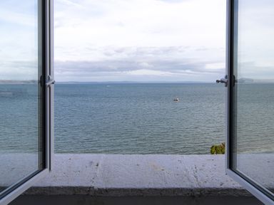 An open window looking out over a body of water with a boat and distant land at No 10 Croft House in Tenby