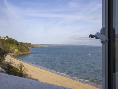 A sandy beach with cliffs and houses on the left and a boat on the ocean seen through a window at No 10 Croft House in Tenby