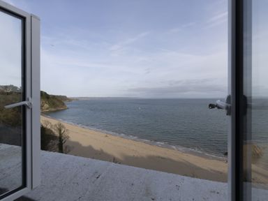 View of a sandy beach and ocean seen through open windows at No 10 Croft House in Tenby