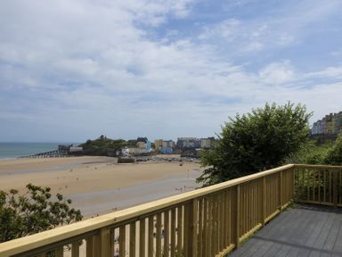 A wooden balcony overlooking a sandy beach with a pier and colorful buildings in the background at No 10 Croft House in Tenby
