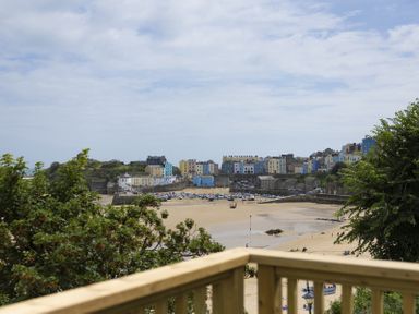 A coastal town with colorful buildings near a sandy beach and moored boats seen from a wooden balcony surrounded by trees at No 10 Croft House in Tenby
