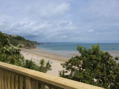 A sandy beach with people, trees in the foreground and hills in the distance at No 10 Croft House in Tenby