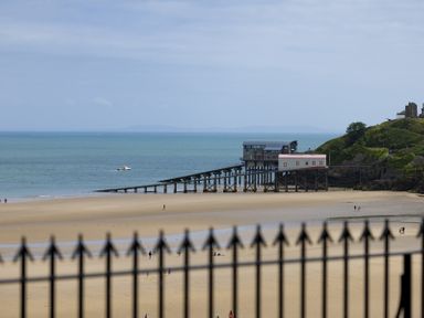 A beach with a pier and buildings on stilts by the sea with a fence in the foreground at No 10 Croft House in Tenby
