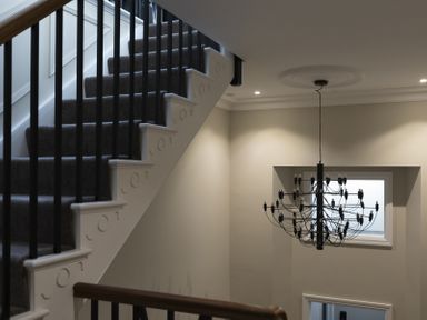 A staircase with dark carpet and black railings next to a large black chandelier and a window at No 10 Croft House in Tenby