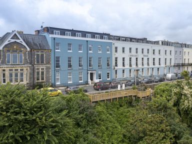 A row of buildings including a blue one labeled Croft House and a white one labeled Fourcroft above greenery and parked cars in Tenby