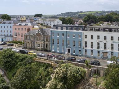 A street with parked cars in front of colorful buildings and greenery in the foreground at No 10 Croft House in Tenby