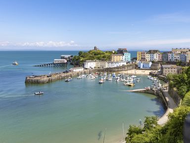 A harbor with boats, colorful buildings, a pier, and a hill with a small structure at No 10 Croft House in Tenby
