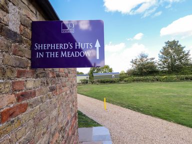 A sign for Shepherd's Huts in the Meadow with a pathway at Magnolia in Grimsby
