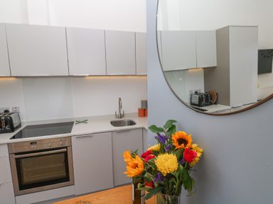 A modern kitchen with grey cabinets an oven a sink a toaster and flowers on a table at Azure Retreat at Una in Carbis Bay near St Ives
