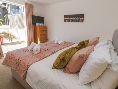 A bedroom with a bed with pillows and rolled towels a chest of drawers with a television and a door leading to an outdoor patio at Azure Retreat at Una in Carbis Bay near St Ives