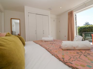 A bedroom with a bed with rolled towels on a patterned blanket a mirror wardrobe doors and an open window with curtains at Azure Retreat at Una in Carbis Bay near St Ives