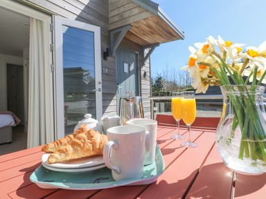 A patio table with croissants mugs orange juice and a vase of flowers outside a wooden house at Azure Retreat at Una Carbis Bay near St Ives