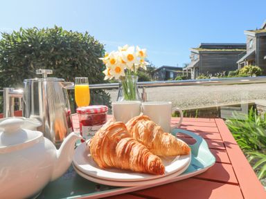 A breakfast setup with croissants, jam, tea pot, coffee pot, two mugs, orange juice, and flowers on a table outdoors at Azure Retreat at Una in Carbis Bay near St Ives