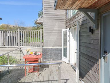 An outdoor wooden deck with a red table and chairs and a glass door leading into a building at Azure Retreat at Una Carbis Bay near St Ives