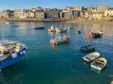 A harbor with small boats floating on the water and buildings along the shore at Azure Retreat at Una Carbis Bay near St Ives